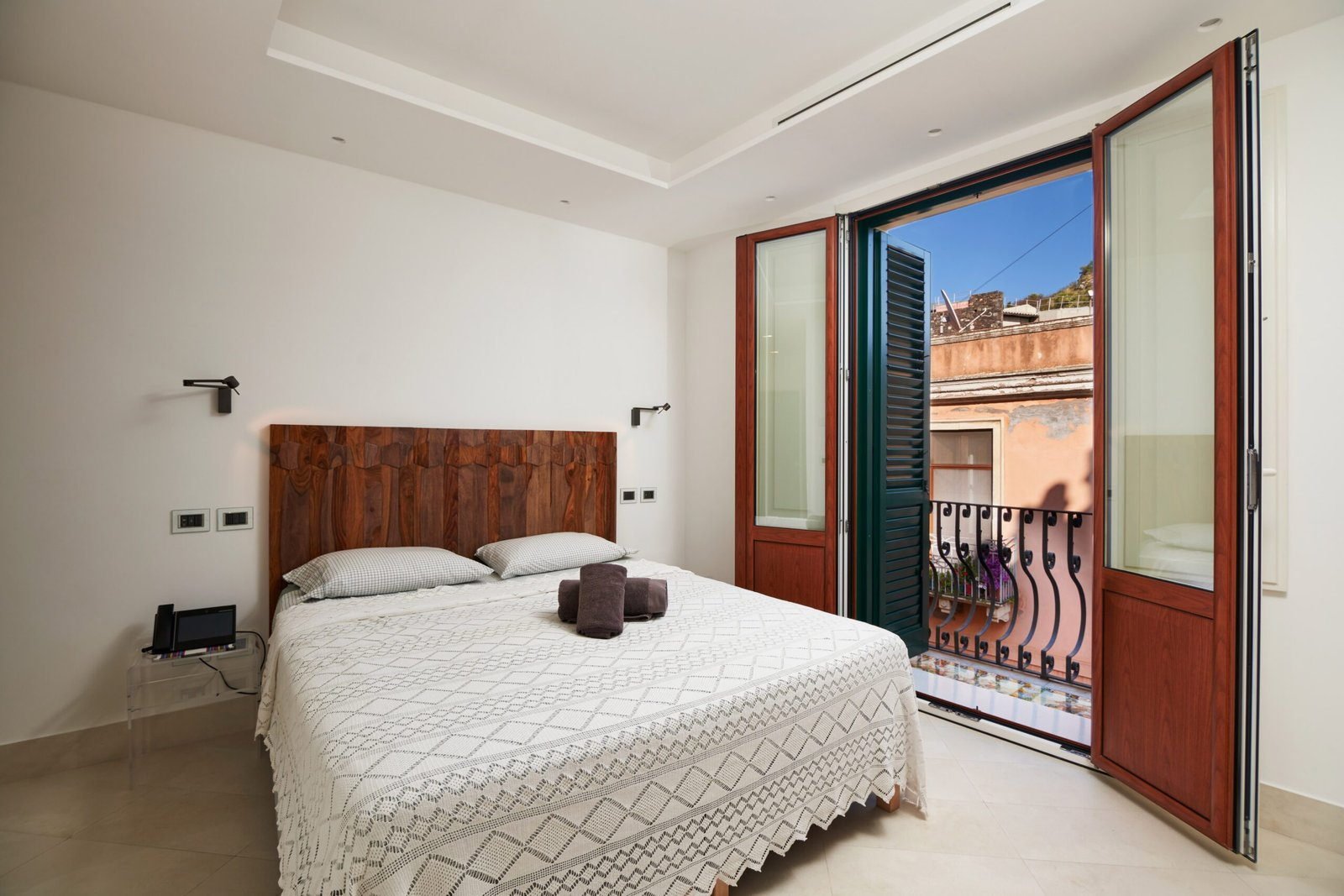 King Standard room with a walnut headboard and balcony doors opening onto green shutters